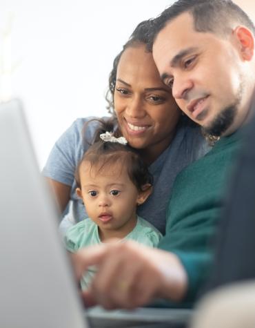 two adults on laptop with young child on lap
