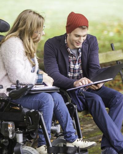 2 young adults in park looking at laptop.