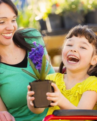 Smiling girl in wheelchair with flower in pot and adult. 