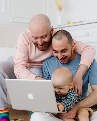 Two adults hugging and holding baby while looking at a laptop.