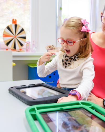 Young child leaning to use a digital table device to communicate.