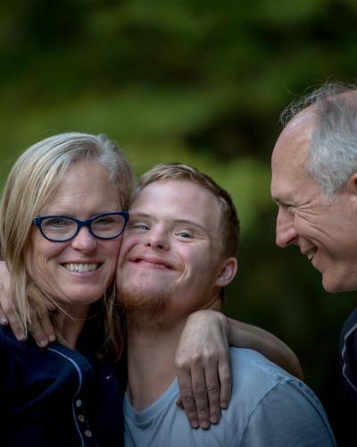 Youth smiling and hugging two adults.