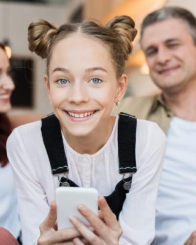 Youth holding cell phone, two adults in the background.